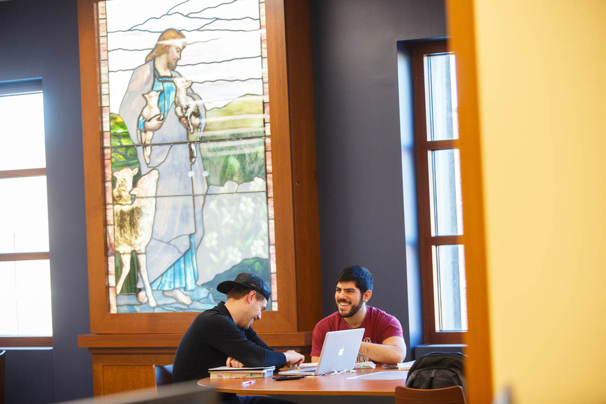 Photograph of two students talking near the stained glass portrait of St. Vincent de Paul in the JTR Library Photograph of two students talking near the stained glass portrait of St. Vincent de Paul in the JTR Library
